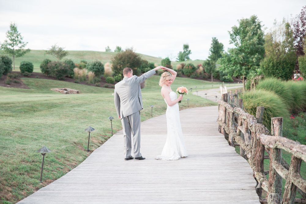A couple shares a playful moment while walking on a wooden boardwalk in a pastoral setting.