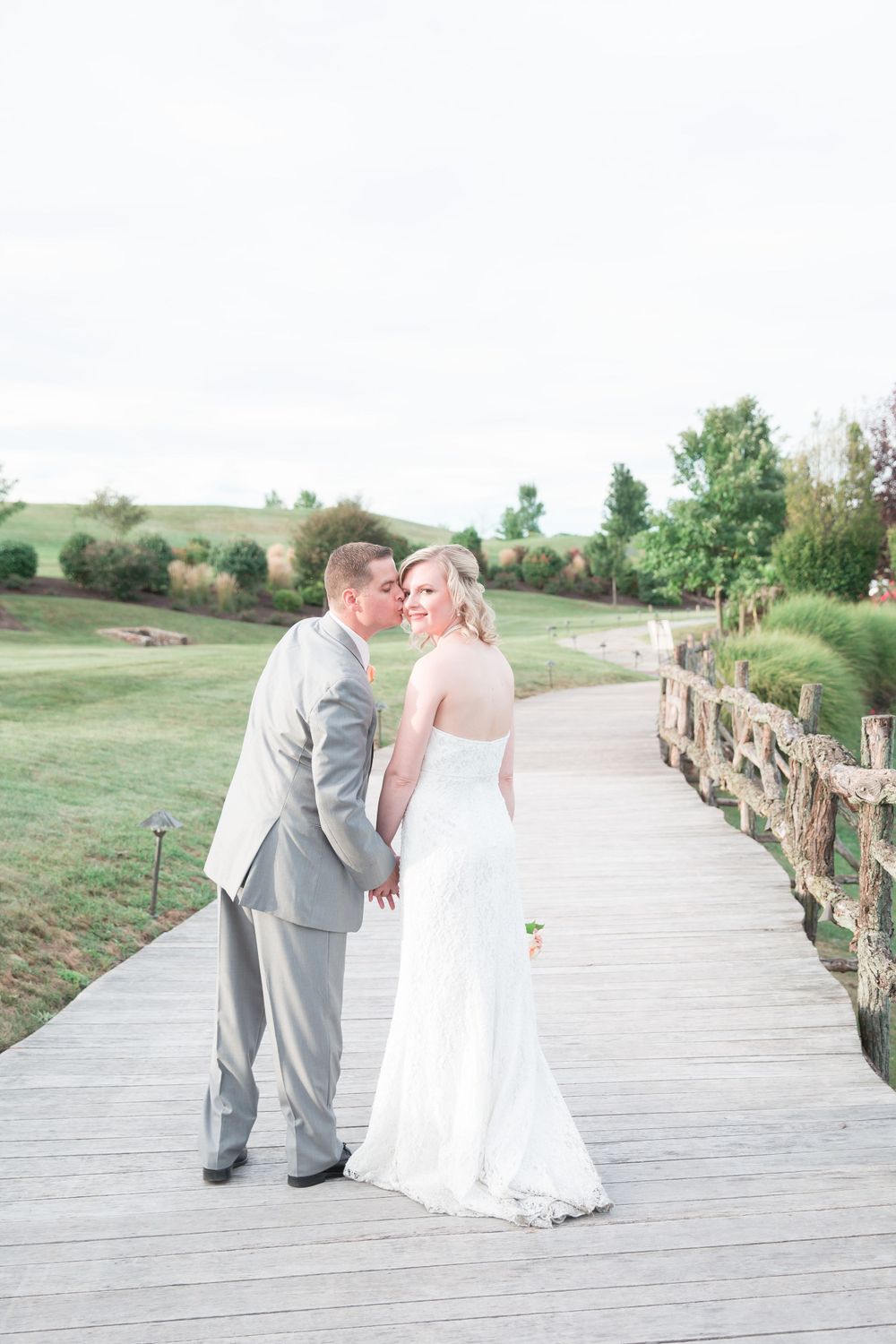 A couple poses on a wooden boardwalk surrounded by rolling hills and greenery.