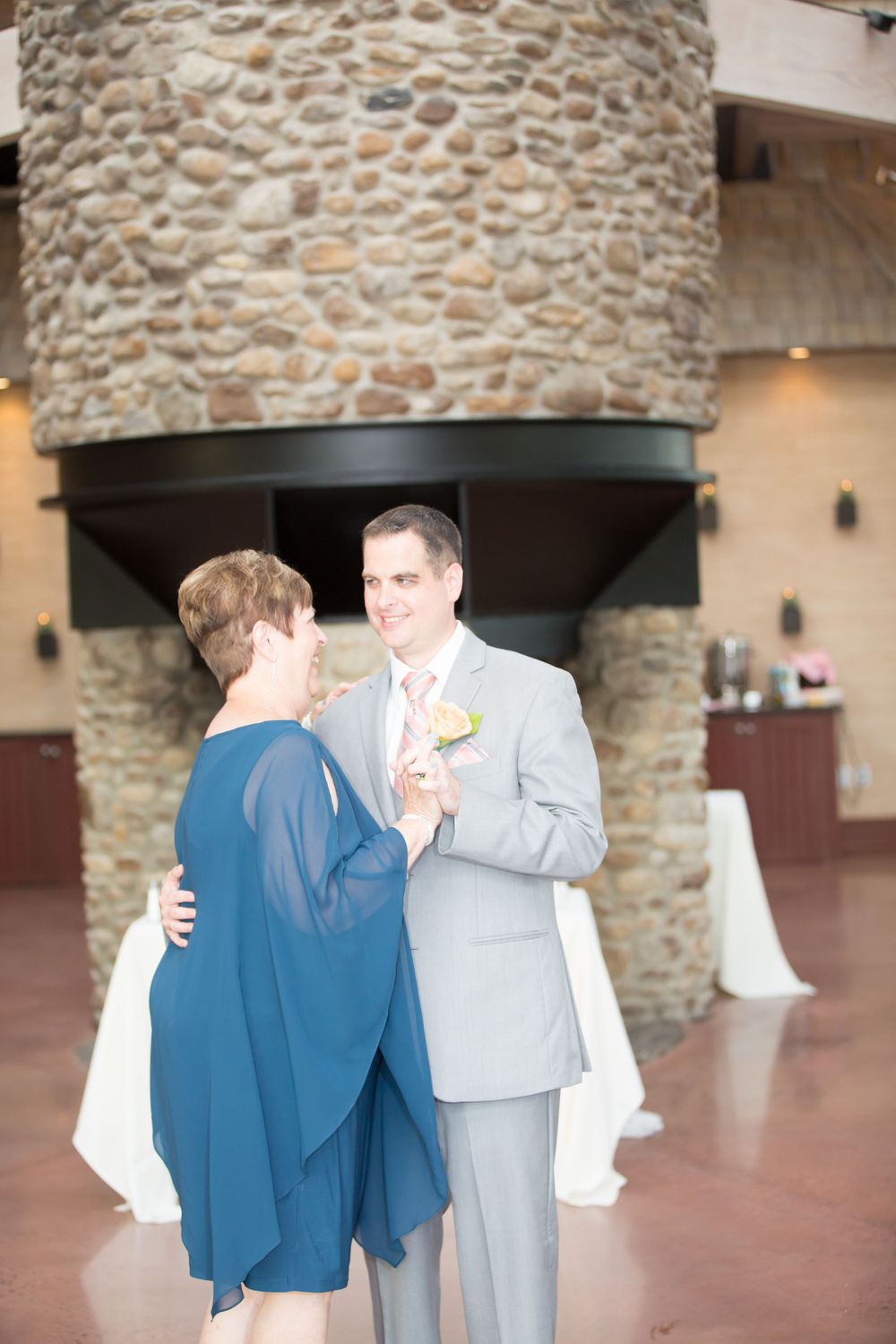 A tender moment between dancers near a grand stone fireplace at a wedding reception.