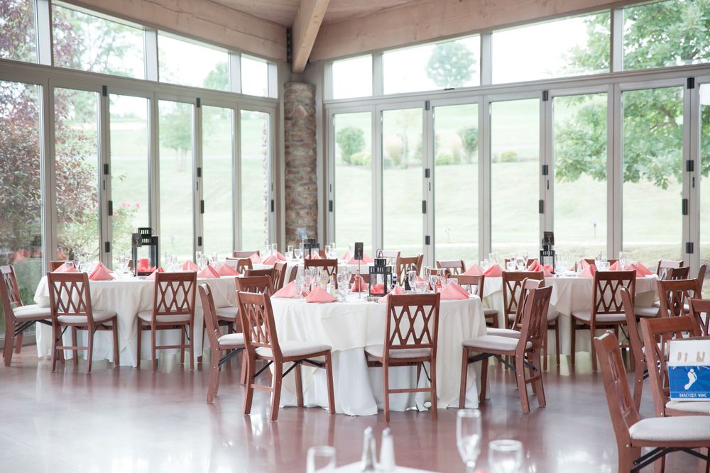 Bright sunlit reception venue with white tablecloths and wooden chairs.