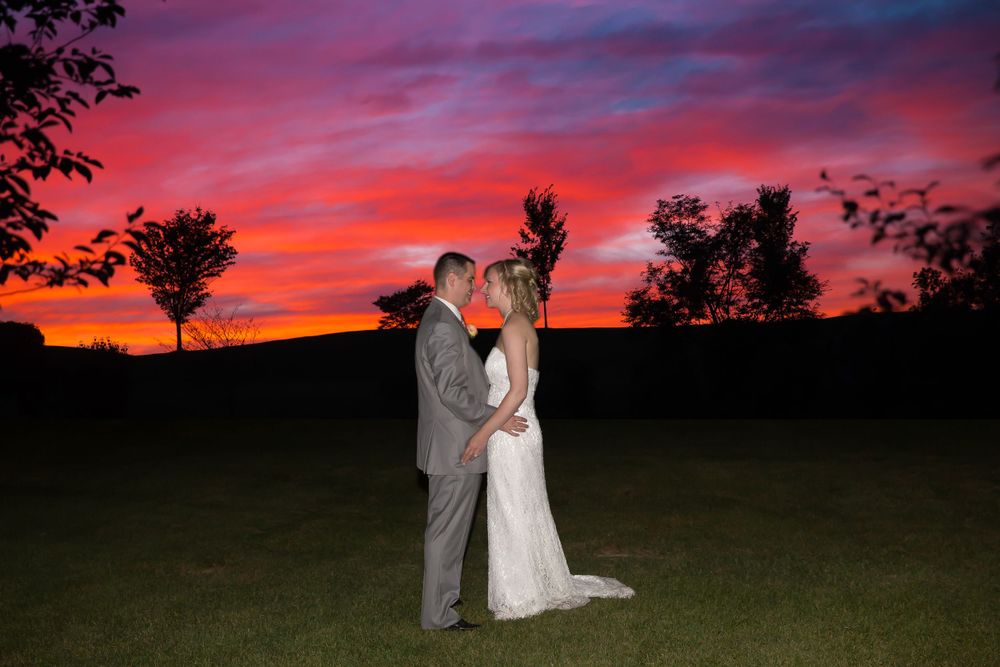 A wedding couple embraces during sunset with vibrant pink and purple sky in the background.