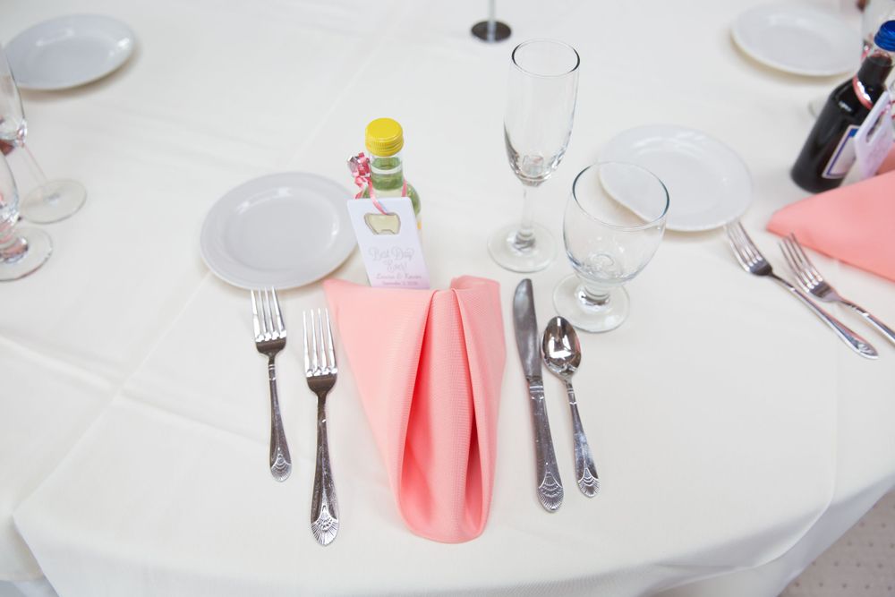 Table setting with coral napkin, silverware, and glassware on white tablecloth.