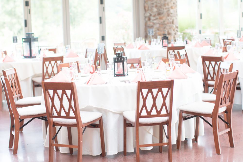 Reception tables set with white linens and wooden lattice-back chairs in an elegant dining room.