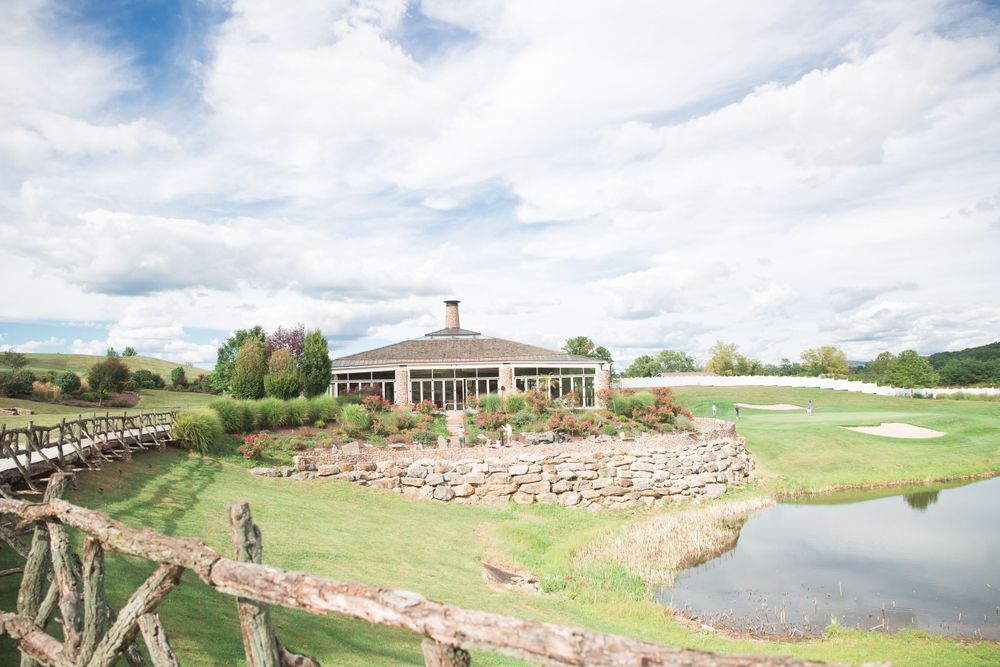 A golf club clubhouse overlooking a pond with stone walls and rustic fencing on a sunny day.