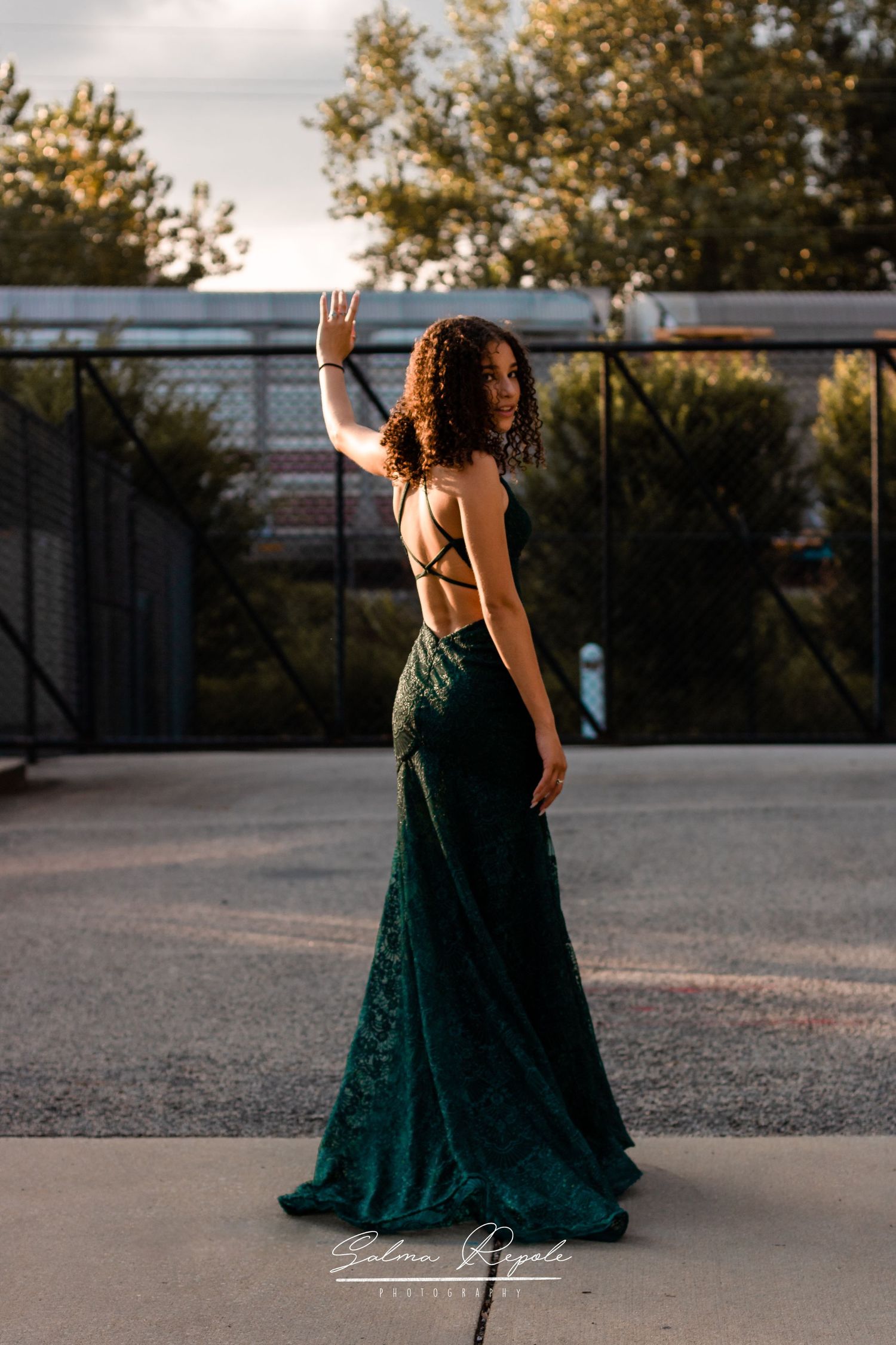 Person in emerald green evening gown twirls gracefully on concrete surface at sunset.