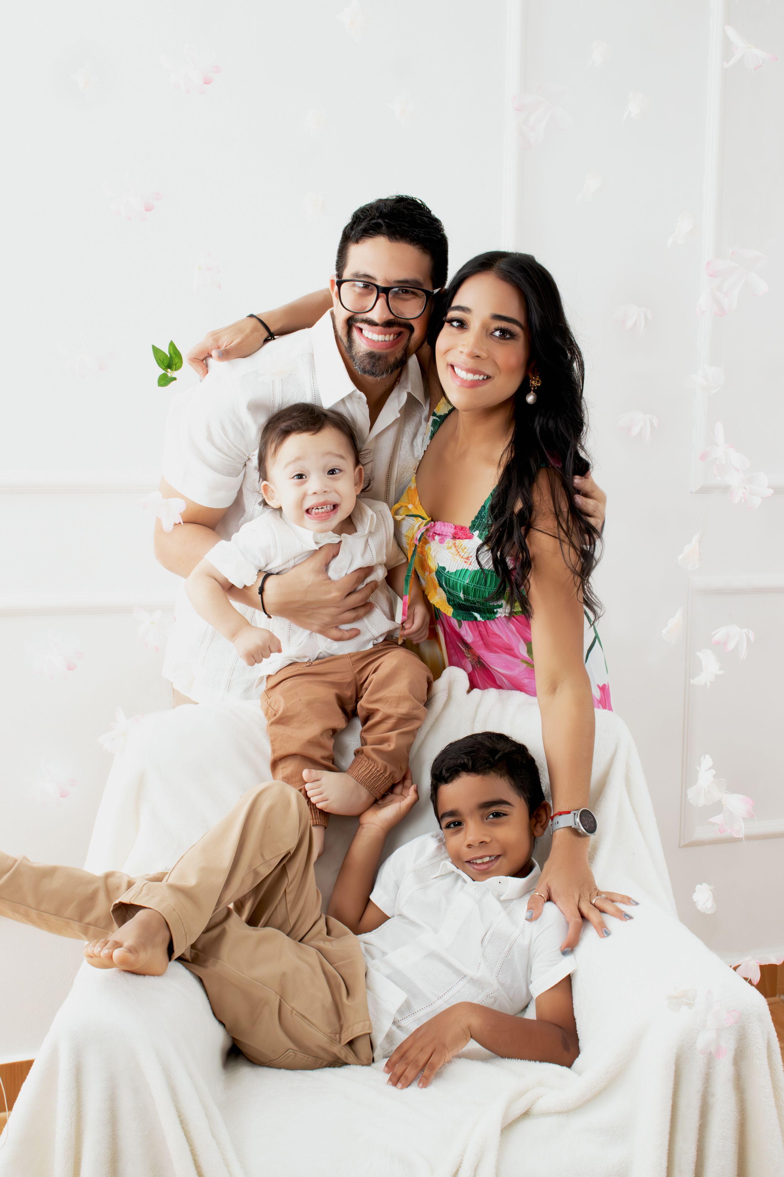 Family with two young children sitting together on a white couch in a bright minimalist setting.