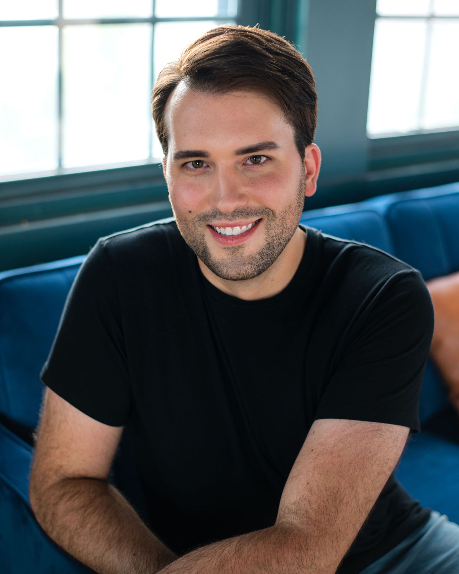 A person in a black t-shirt sits casually on blue seating indoors.