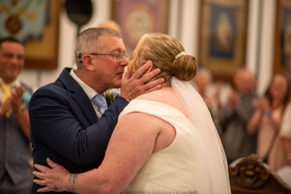 Emotional wedding kiss captured during indoor reception celebration.