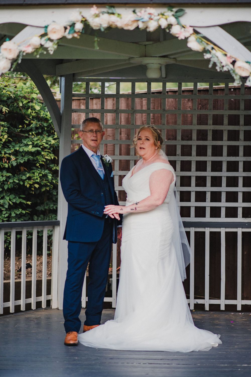 Wedding ceremony under white gazebo decorated with pink floral arch.