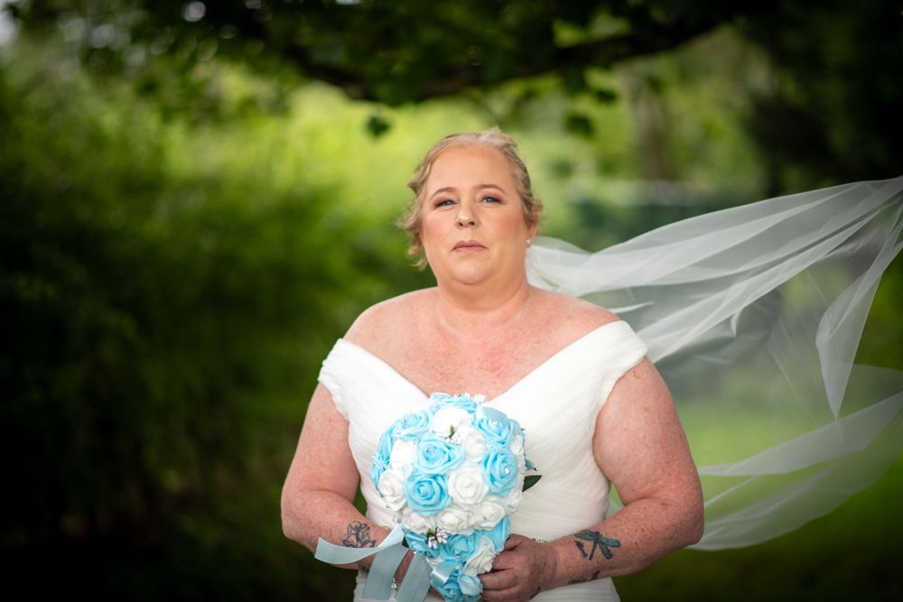 A bride in a white dress holds a blue and white bouquet while standing outdoors.