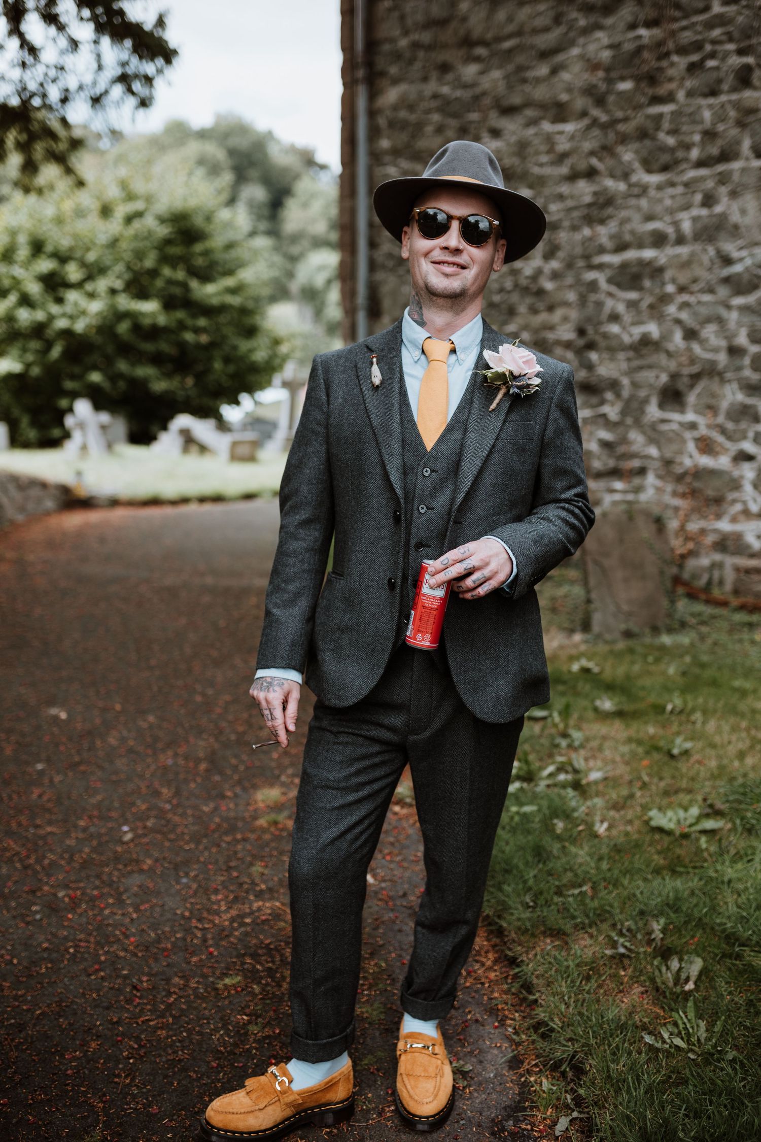 happy groom stood outside church drinking pimms in the church yard