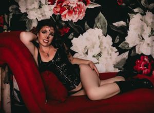 Vintage-style portrait against floral wallpaper with red chaise lounge.