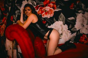 Glamour portrait against floral wallpaper wearing red accent piece.