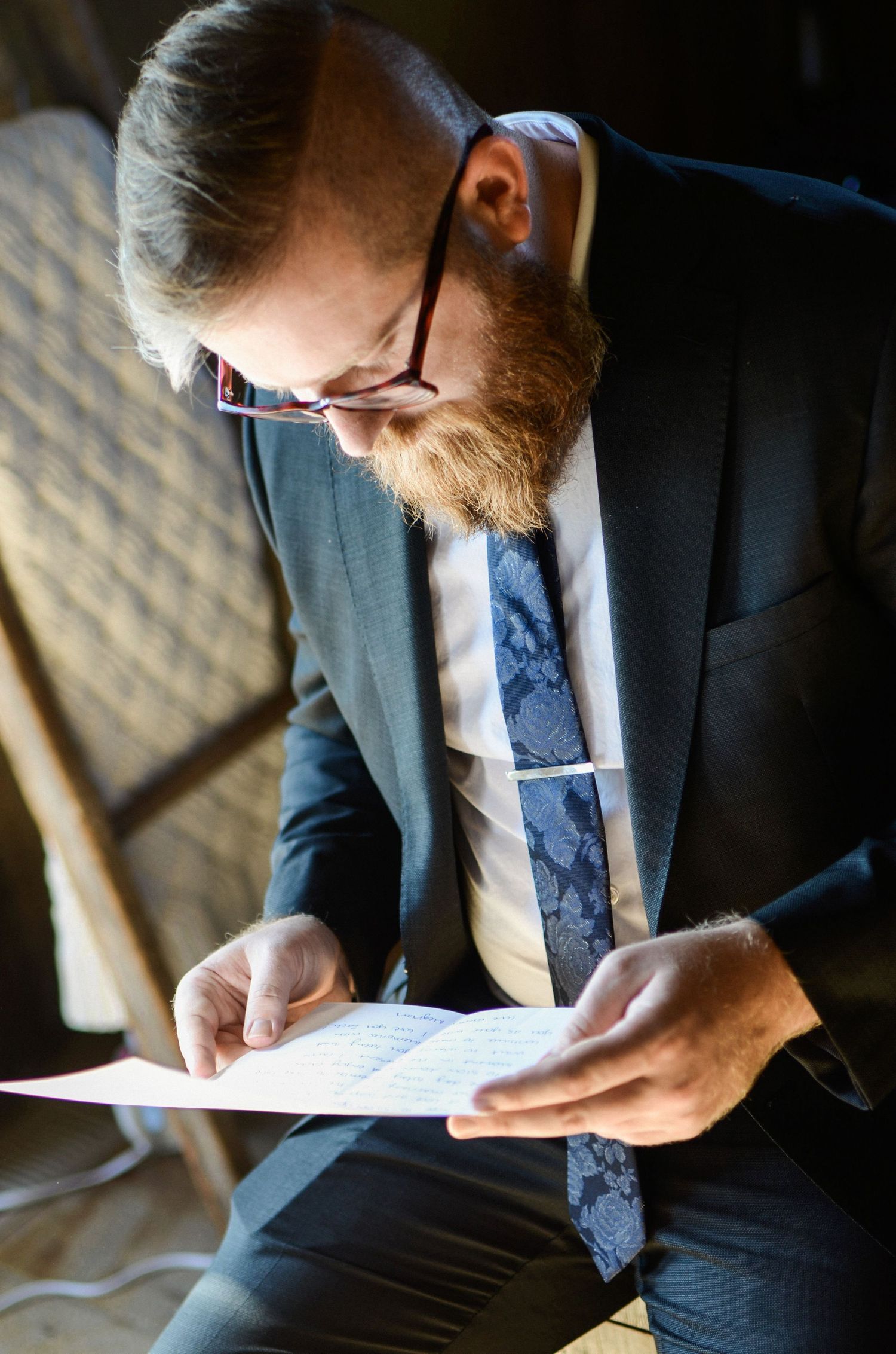 Man in suit writing in notebook under dramatic lighting.