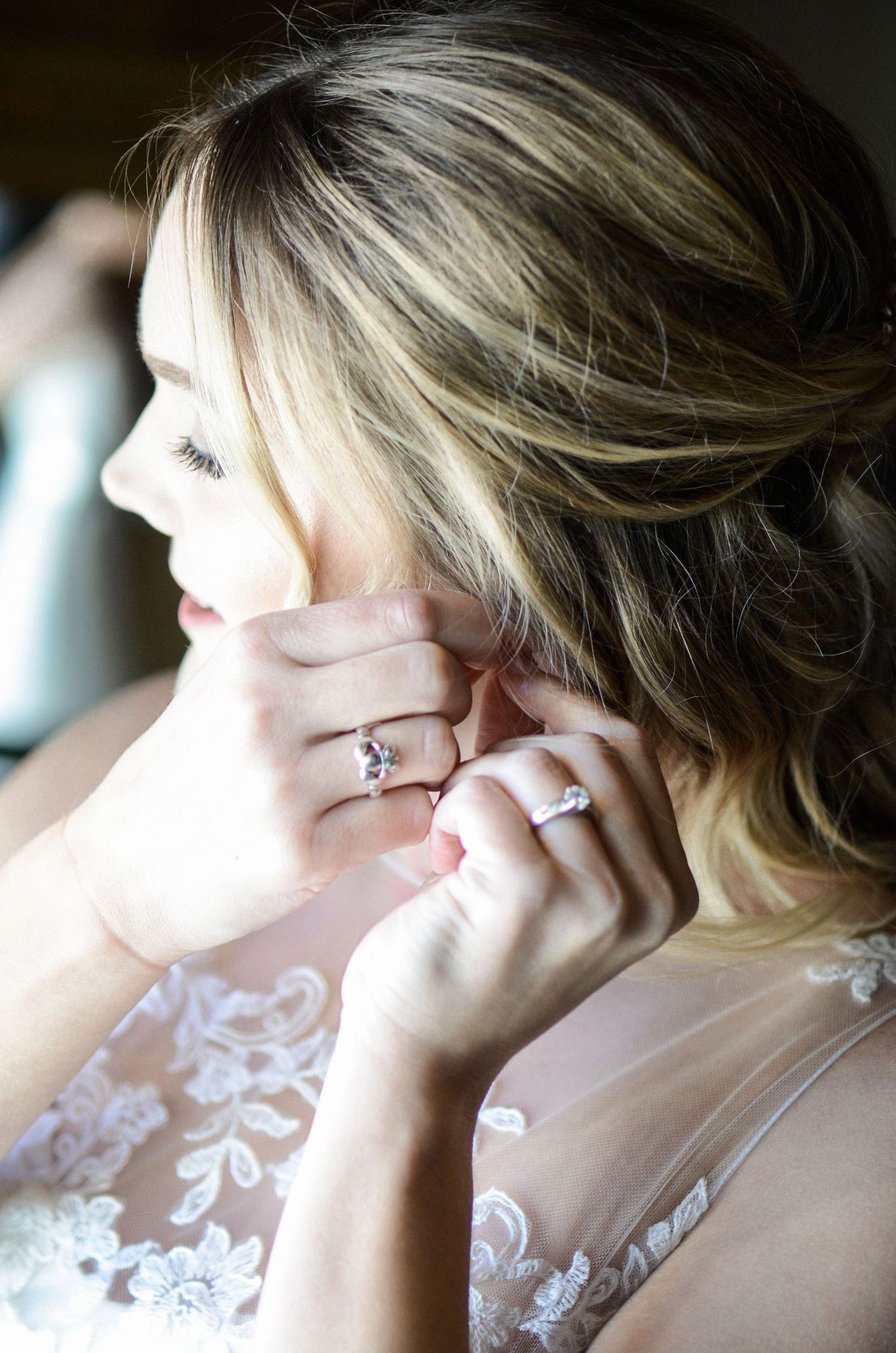 Profile view of a person wearing delicate lace earrings and a white wedding dress.