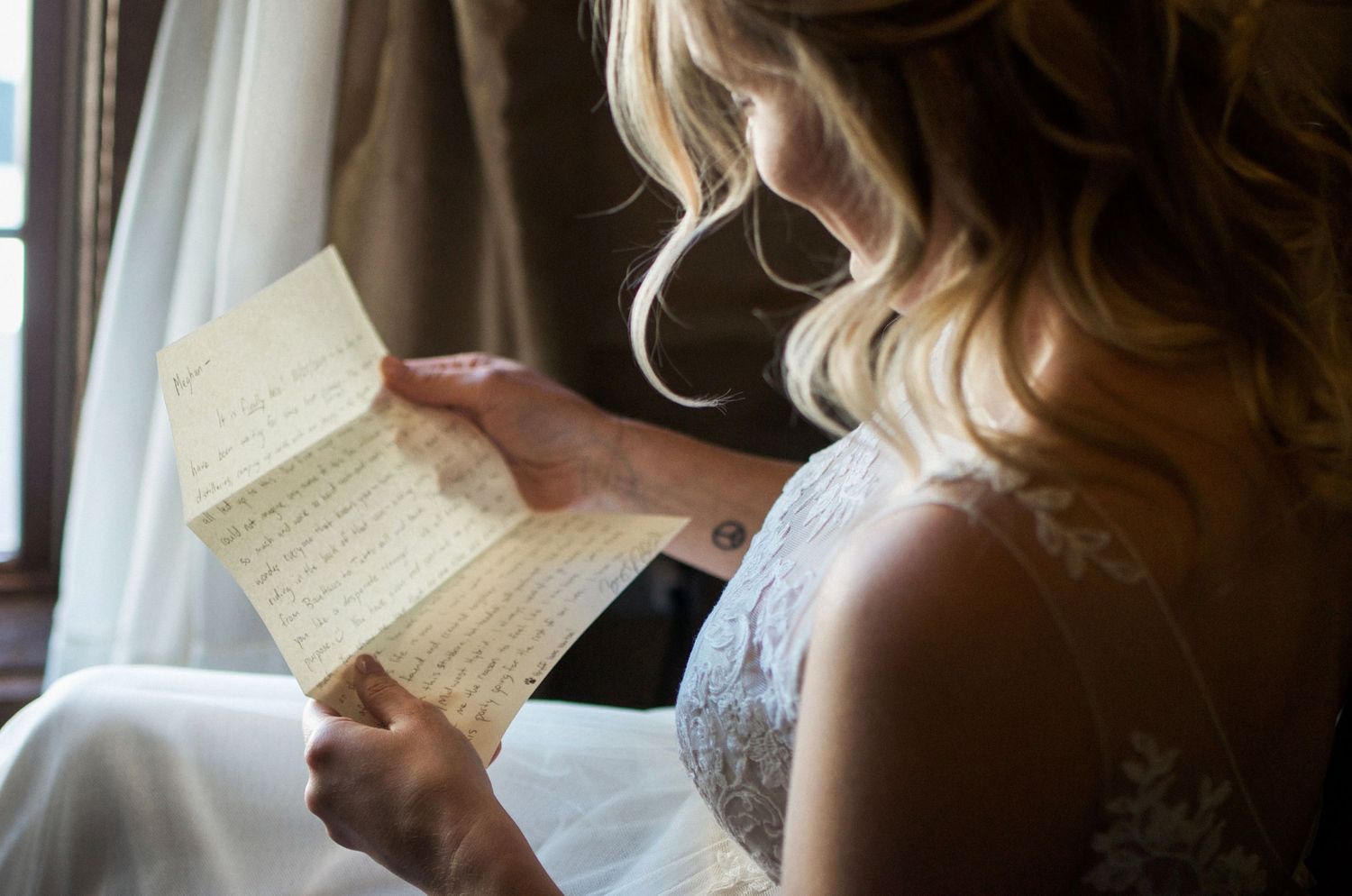 Someone in wedding attire reading a letter or note in natural lighting.