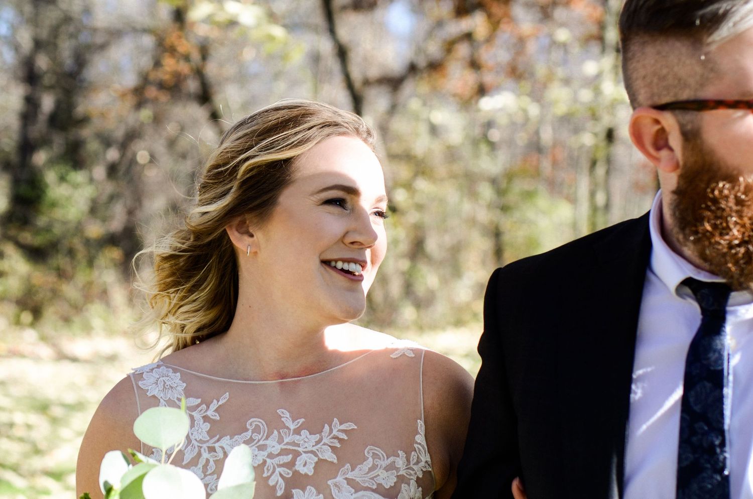A couple in wedding attire share intimate moments under autumn trees.