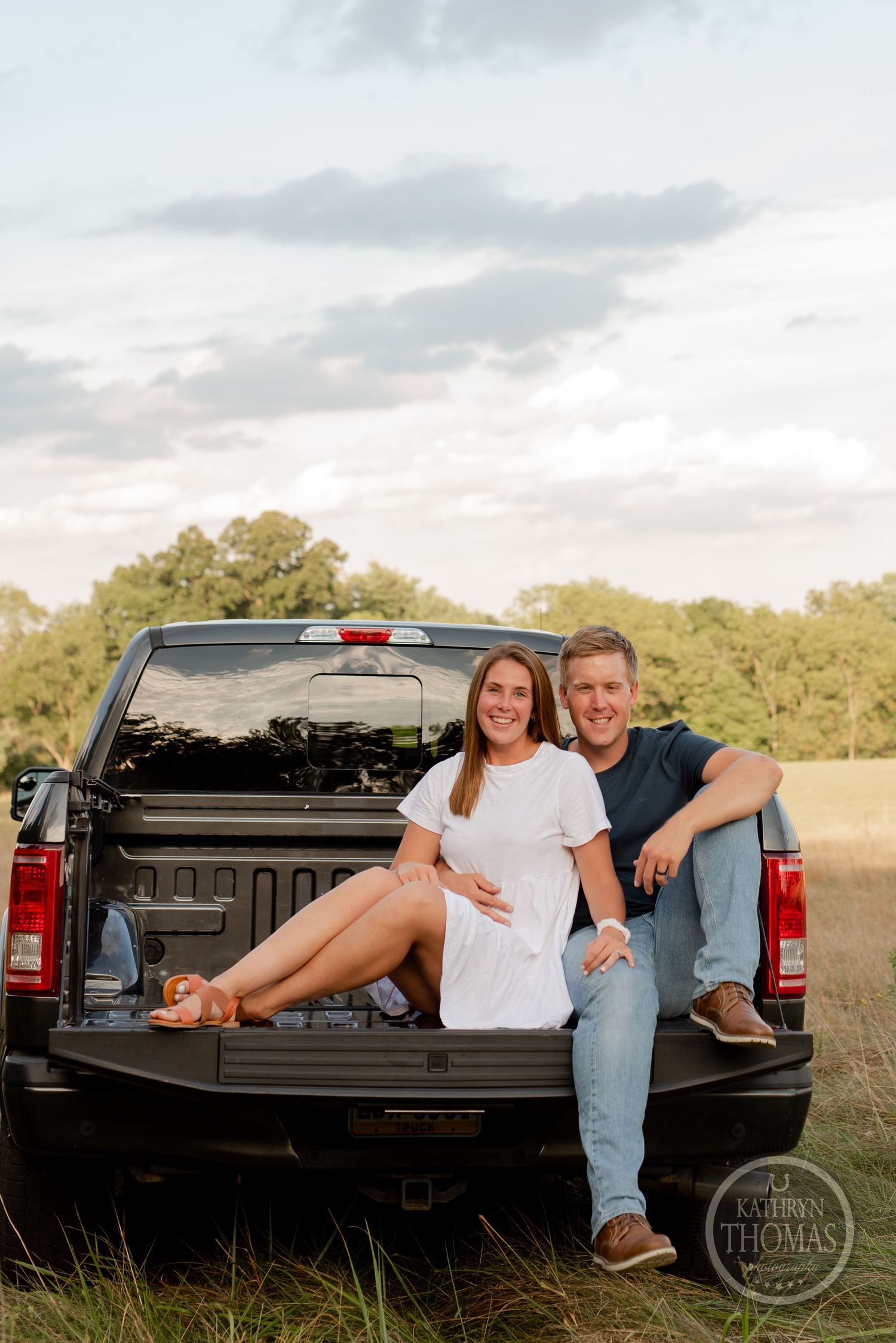 Casual couple poses together in pickup truck bed during golden hour photo session.
