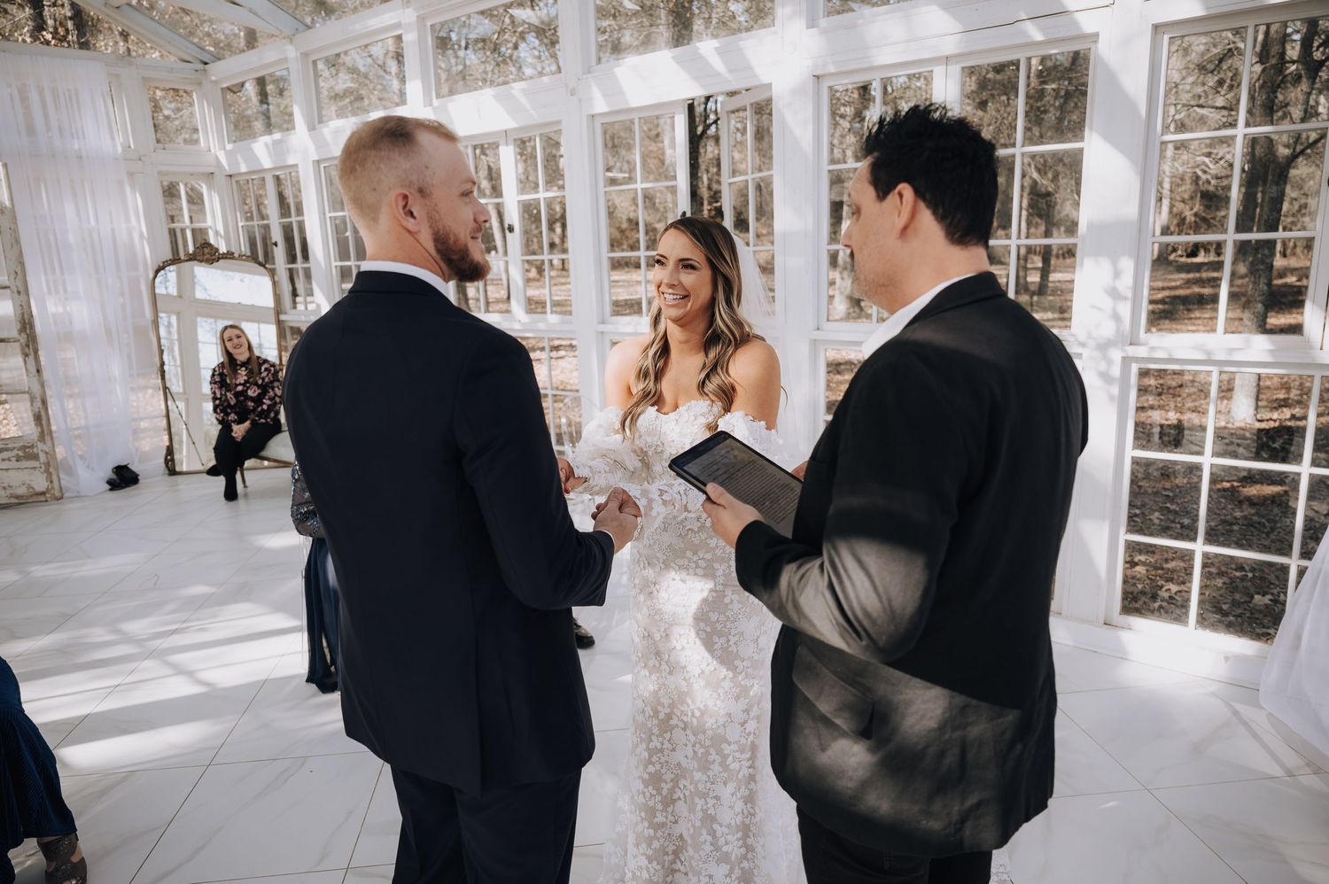 Wedding ceremony taking place in a bright glass-walled venue with natural light streaming in.