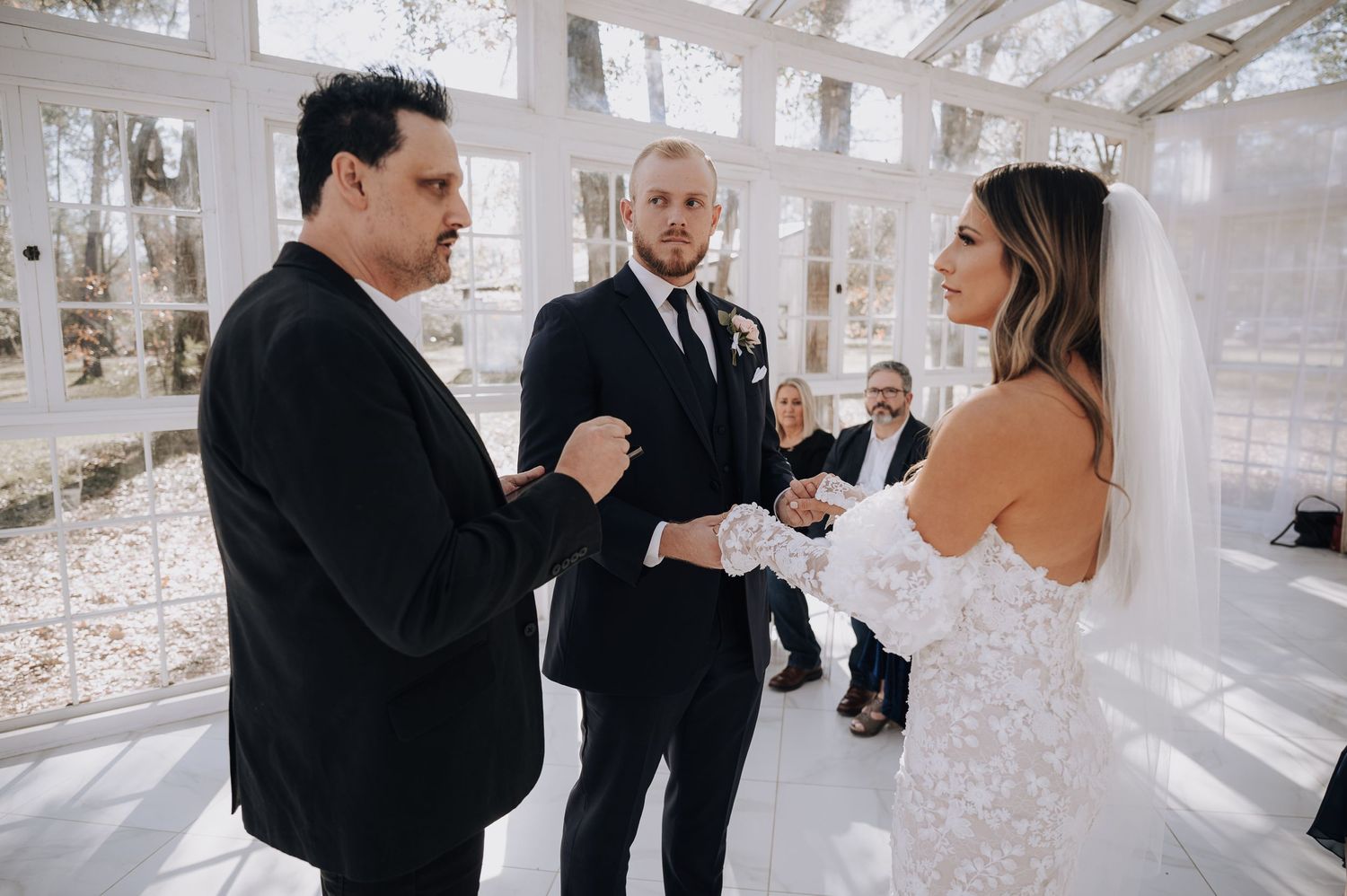 Intimate wedding ceremony in progress inside a sunlit glass conservatory.