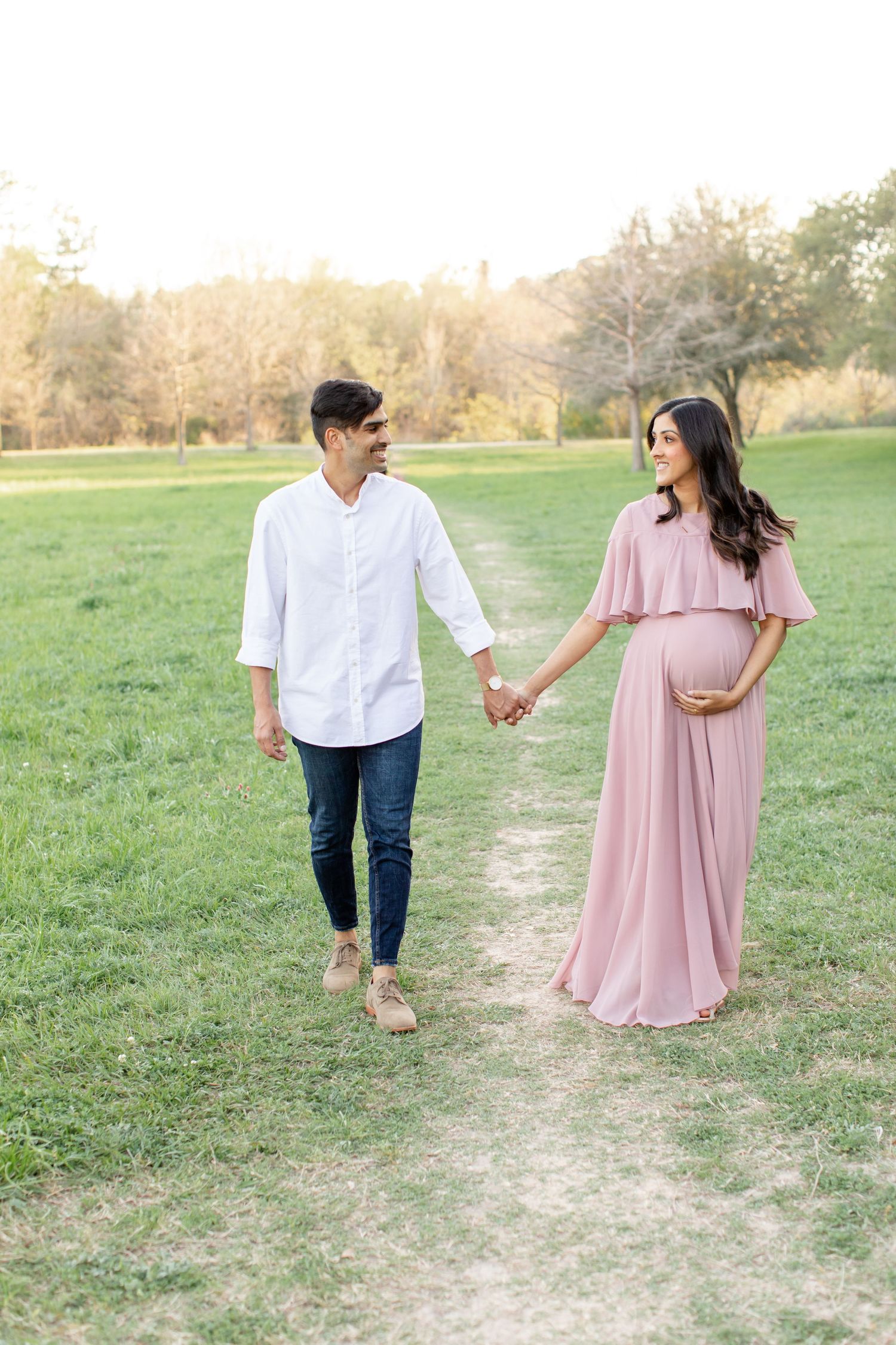 A couple holds hands while walking on a dirt path in a park during sunset.