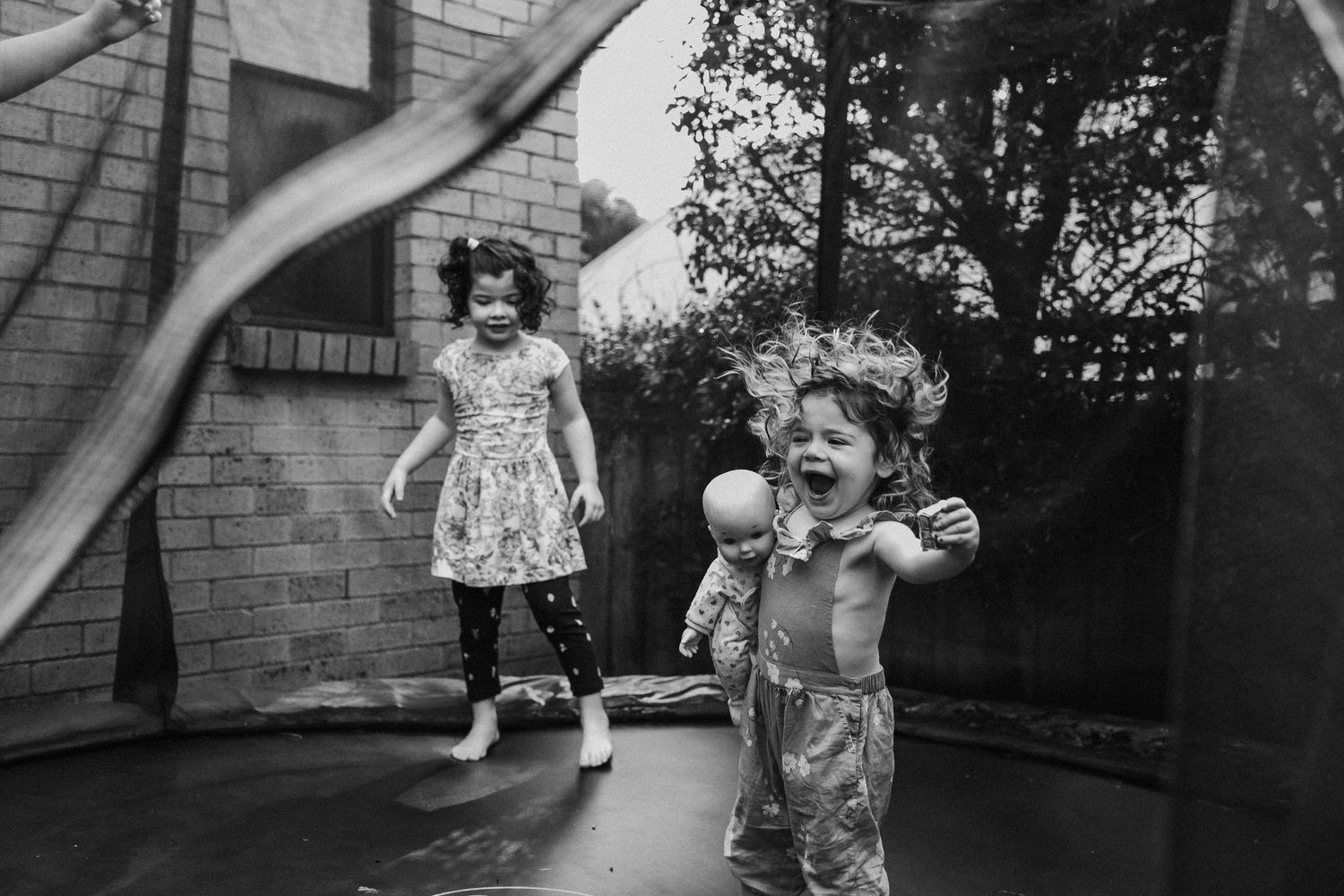 Black and white photo of two young girls playing on a backyard trampoline.
