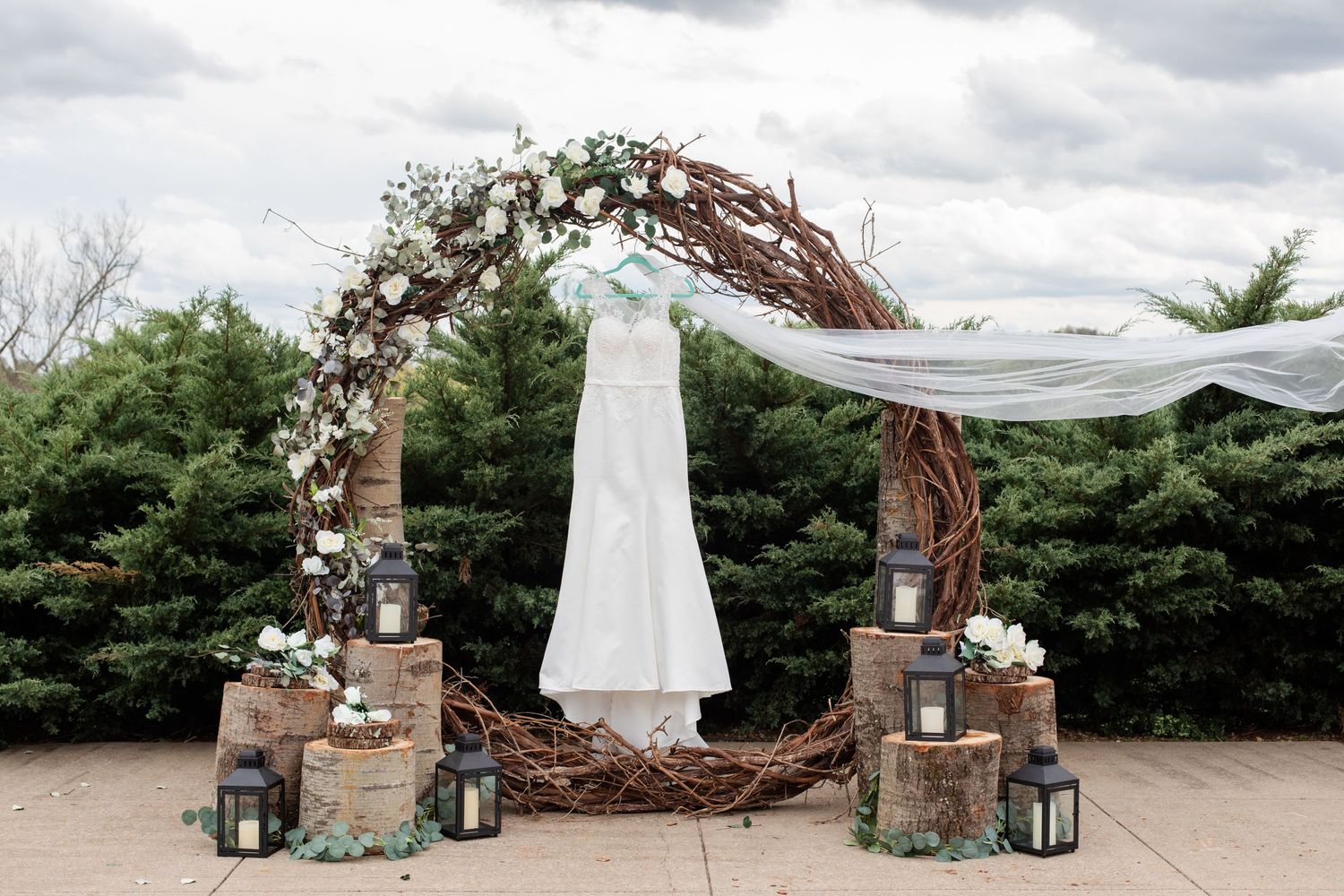 A wedding dress display with rustic stone pillars, lanterns and a natural branch archway.