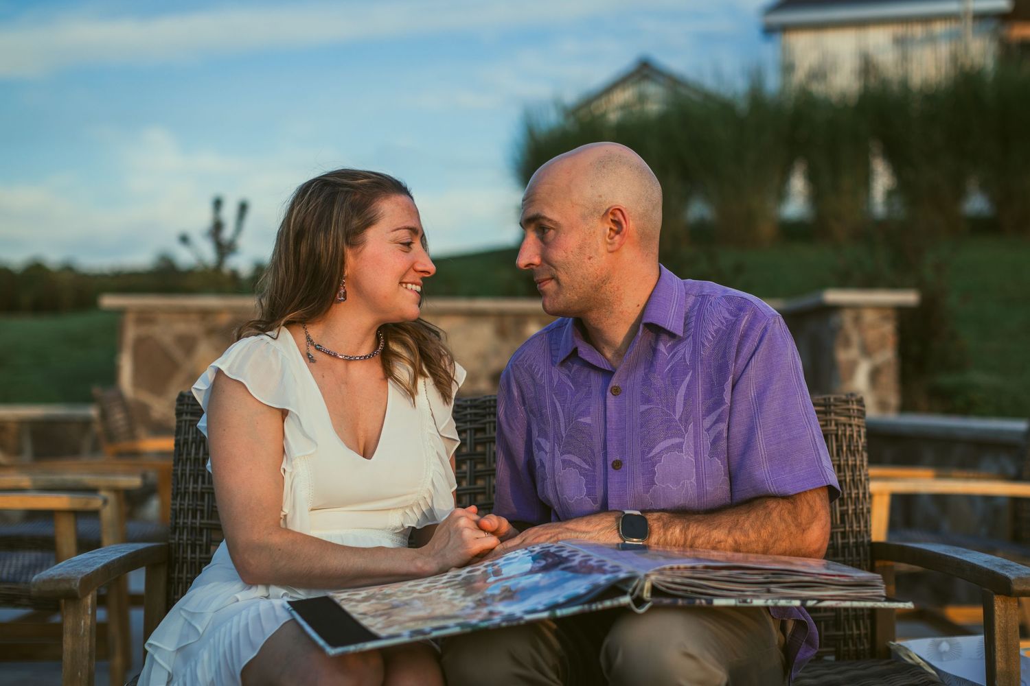 A couple shares a romantic moment while looking at photos together on an outdoor patio at sunset.