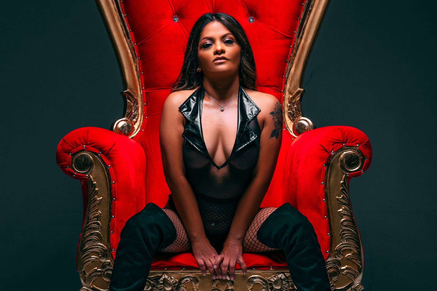 Dramatic portrait on ornate red velvet throne with dark moody lighting.