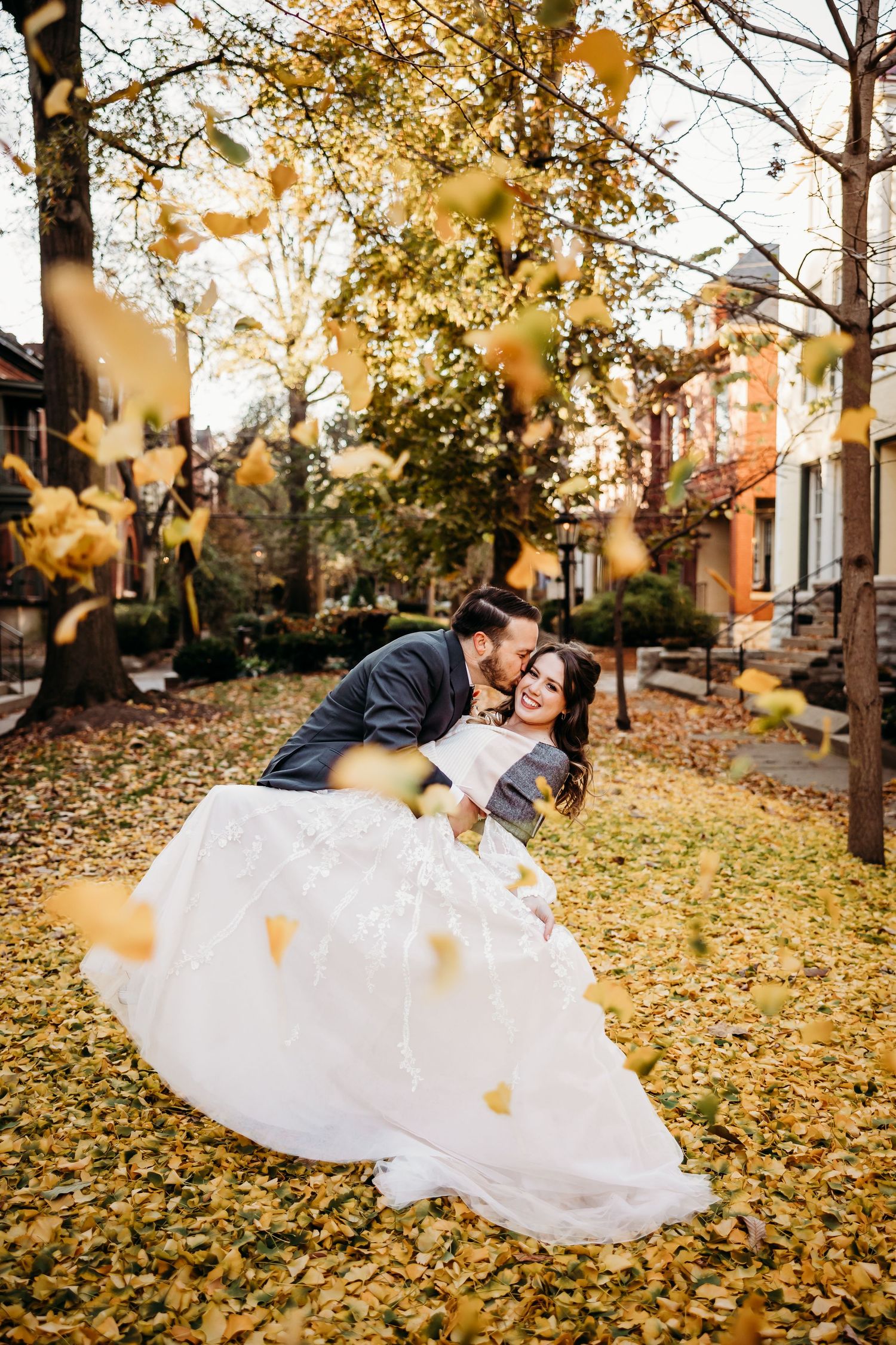 a bride & groom kissing with fall leaves falling around them