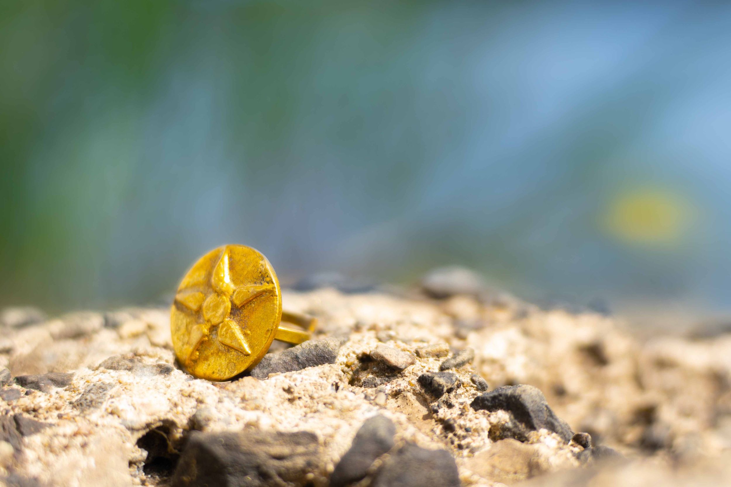 Close-up of a gold star-shaped ring resting on a rocky surface with blurred background.