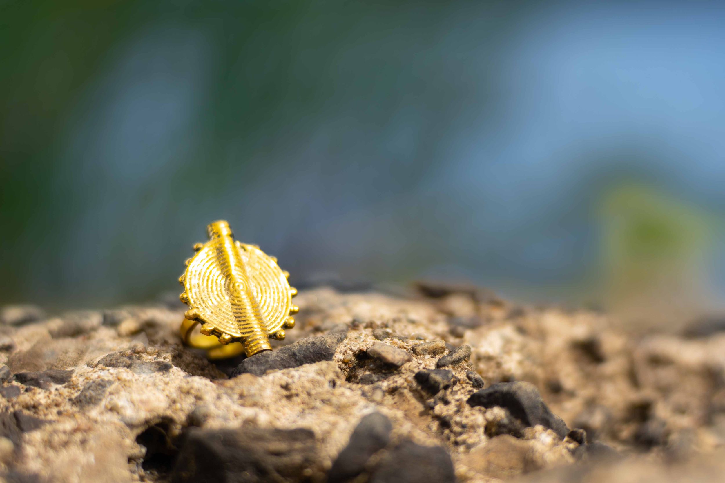Macro shot of a small gold textured ring standing upright on a rocky outdoor surface.