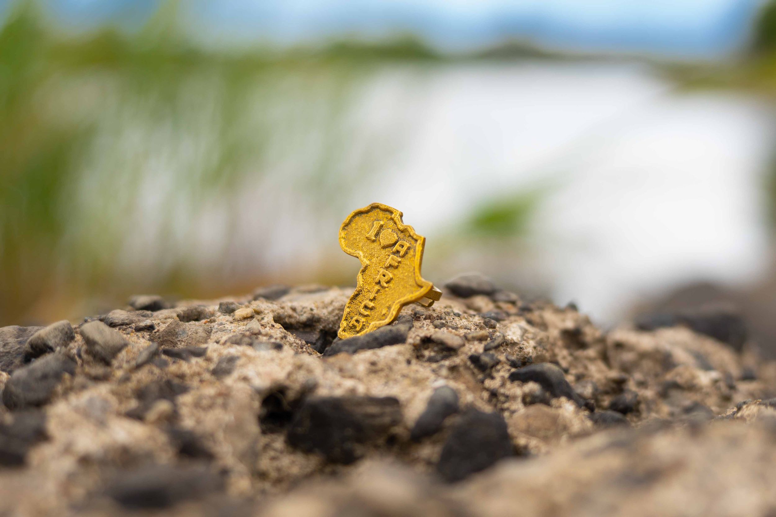 Gold Africa-shaped pin standing on a rocky surface with a blurred natural background.