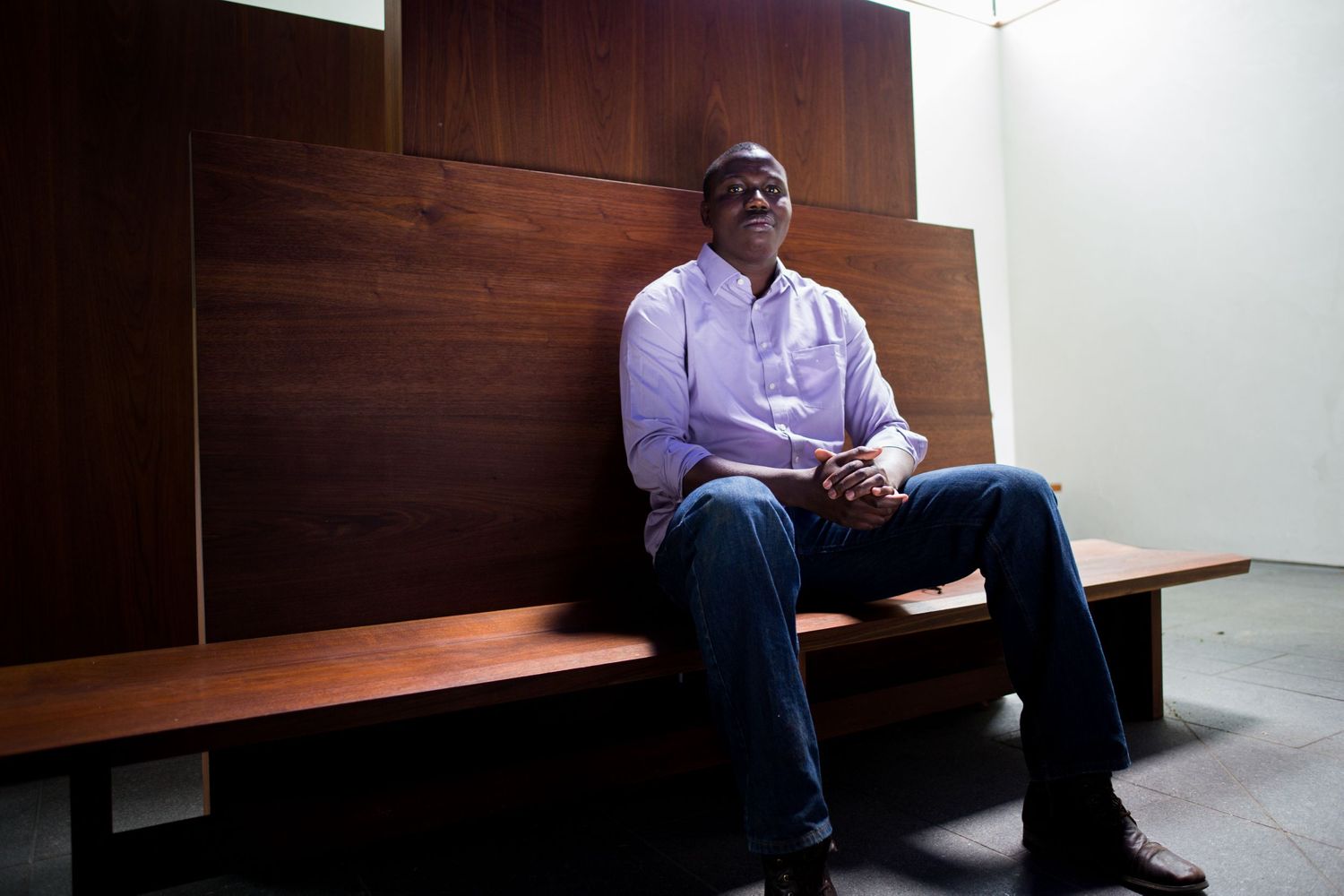 A person sits on a wooden bench in a minimalist interior setting.