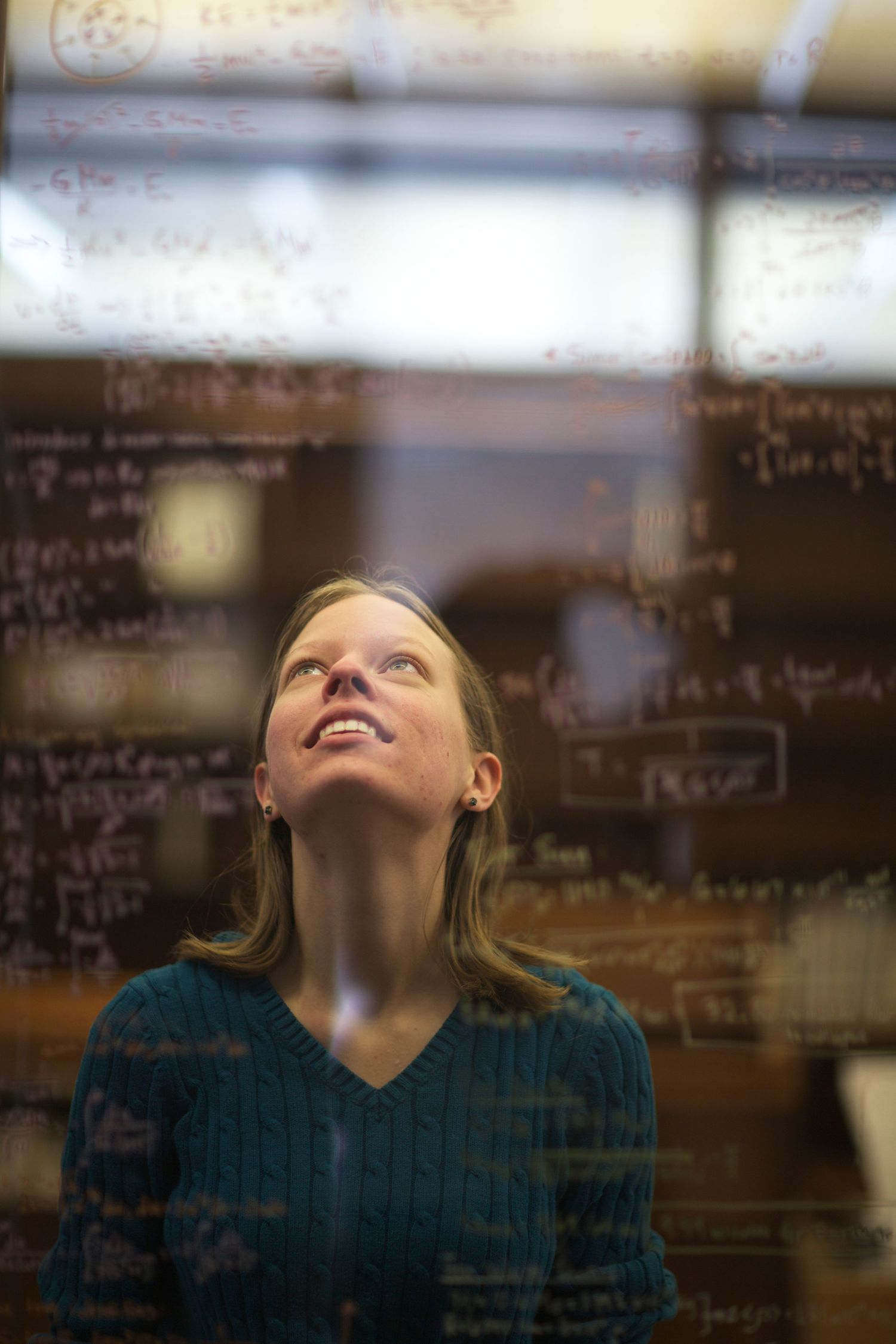A person gazes upward through glass with mathematical equations written on it.