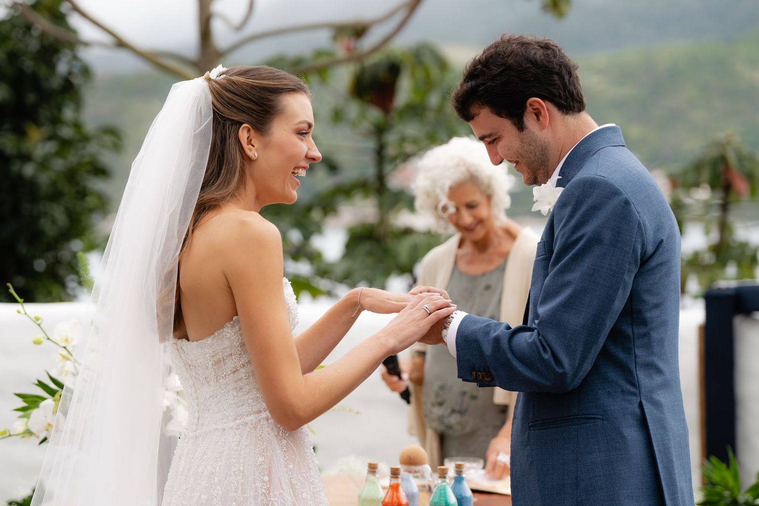 Wedding ceremony exchange of rings against mountain backdrop with guests watching.