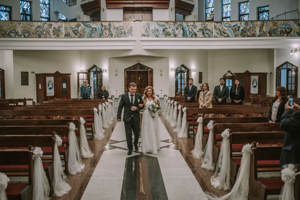 Wedding ceremony setting in a church with white-decorated pews and religious artwork on the walls.