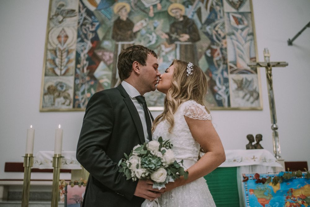 Wedding moment captured in church with religious artwork and stained glass windows in background.