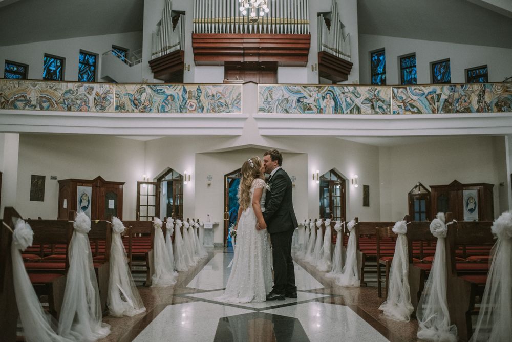 Wedding ceremony in a church sanctuary with white-decorated pews and organ pipes above.