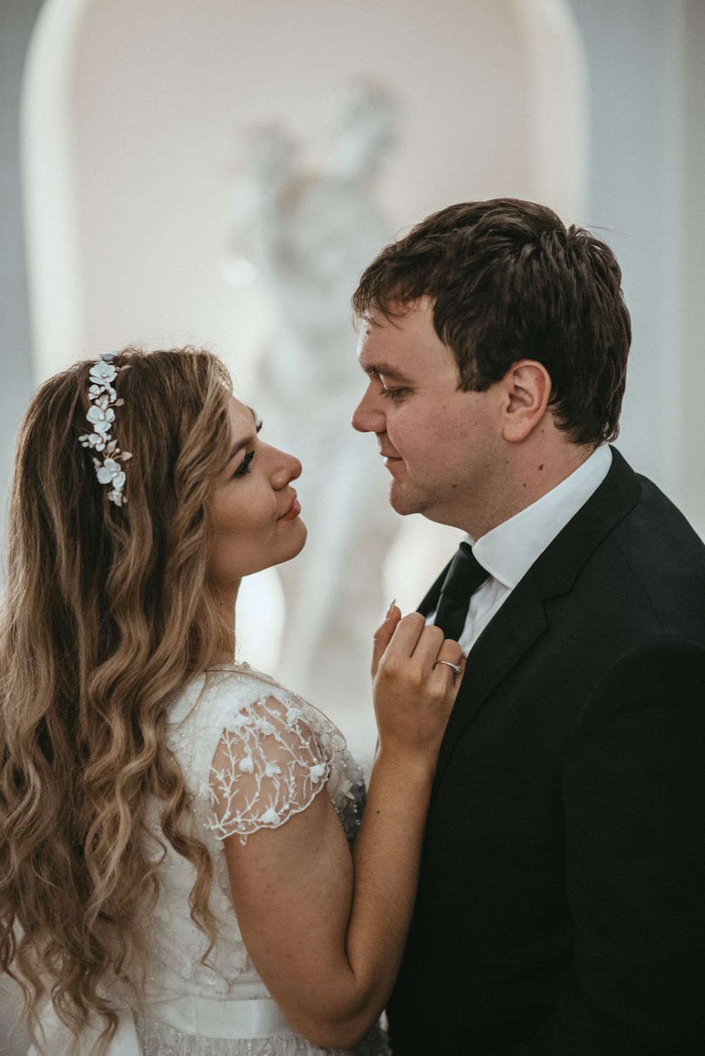 Intimate moment captured against white walls with soft lighting and formal attire.