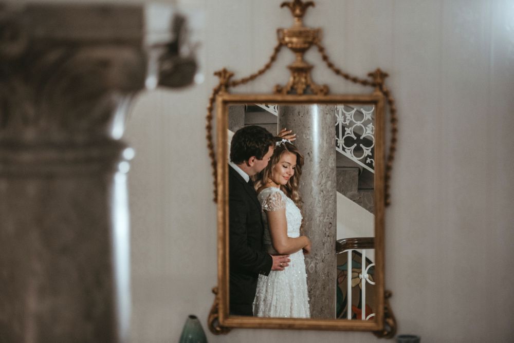 Romantic reflection in an ornate gold mirror showing formal attire in a classic setting.