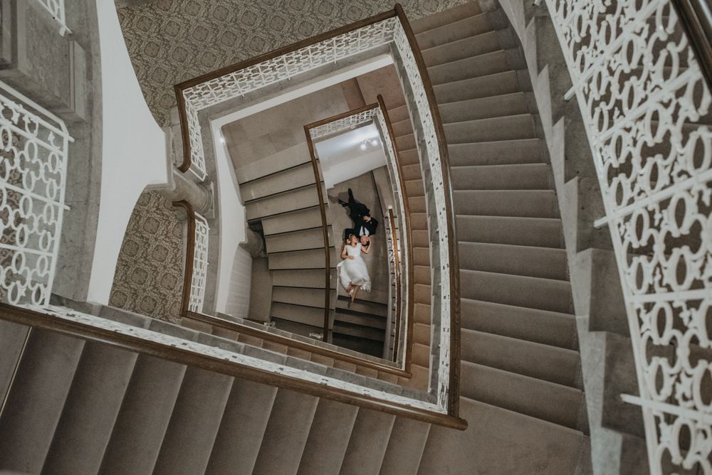Looking down a spiral staircase with ornate white details and curved brown steps in an elegant interior.