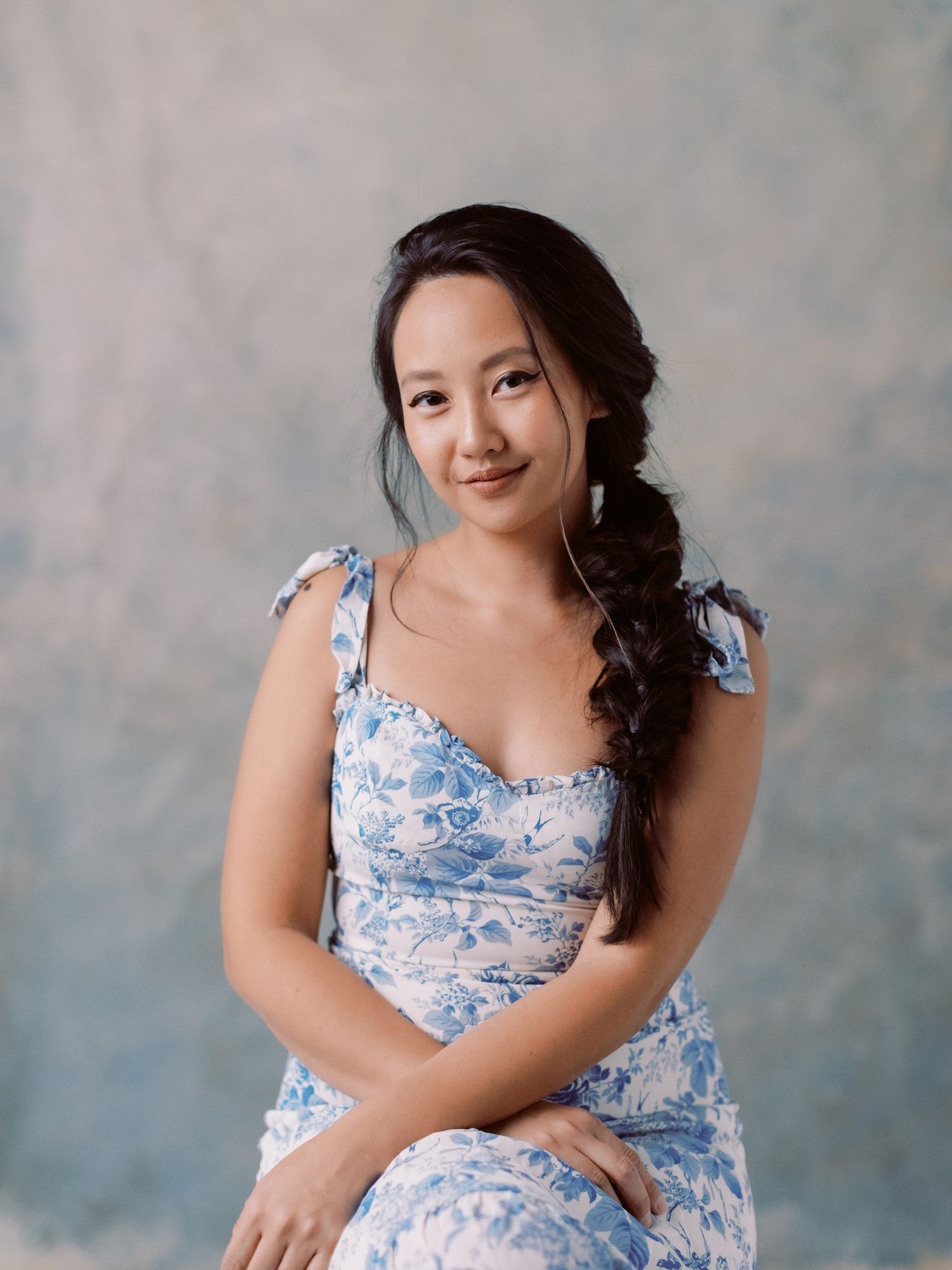 Woman in a blue floral dress poses against a textured backdrop.