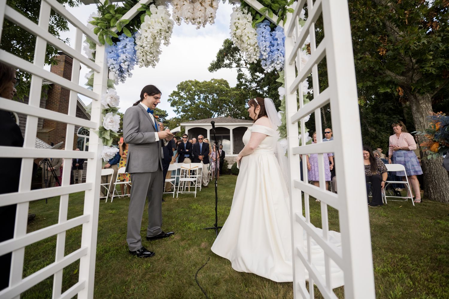 Wedding ceremony setup with white arbor and chairs arranged on a beautiful lawn.