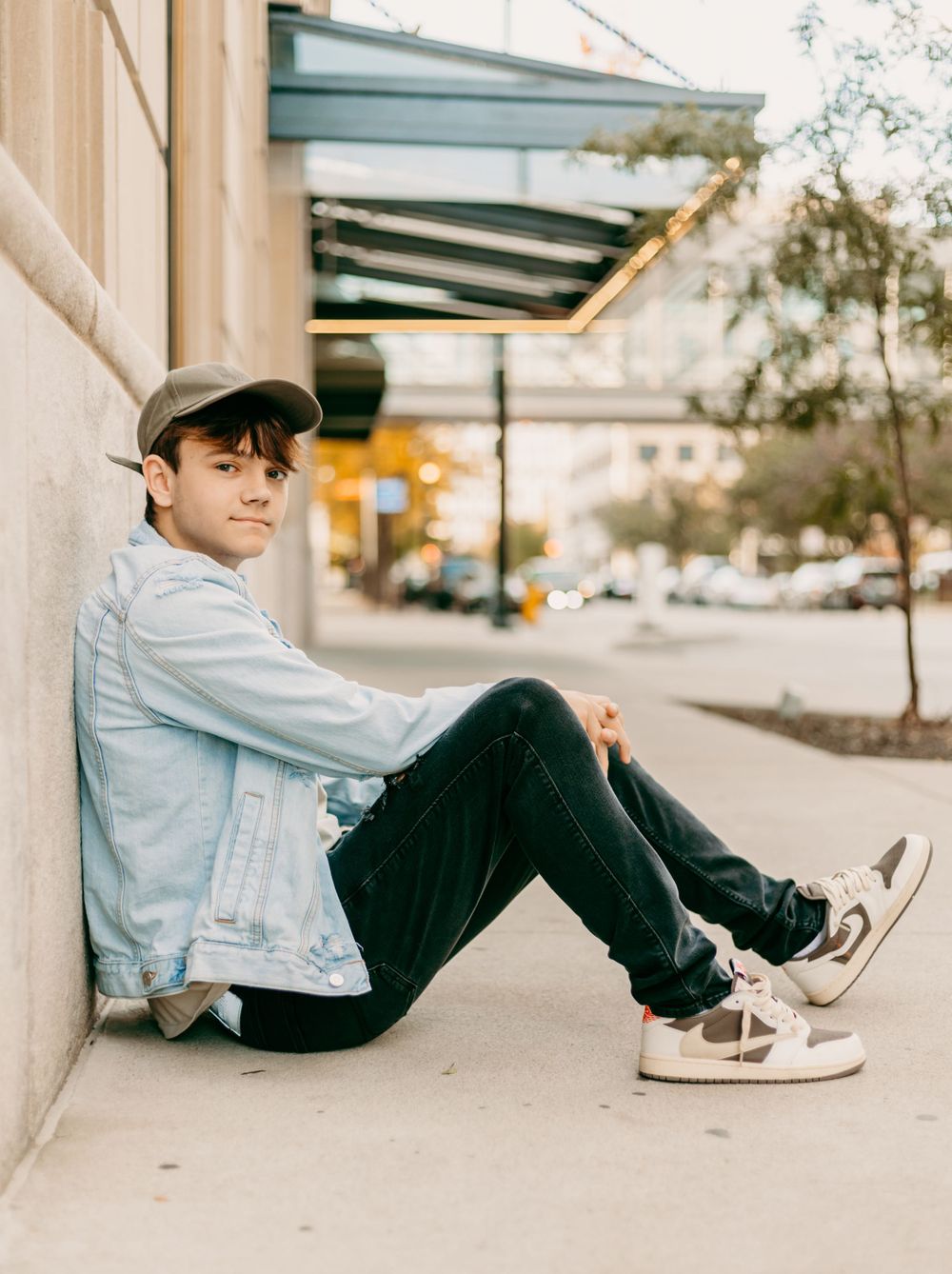 Casual street style portrait against white wall with person sitting on ground.