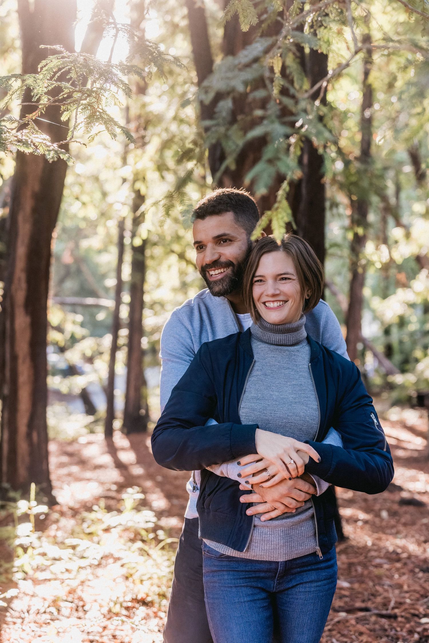 A couple smiling and embracing while enjoying a day in the redwood forest.