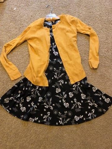 Yellow cardigan and floral black dress laid out on beige carpet.