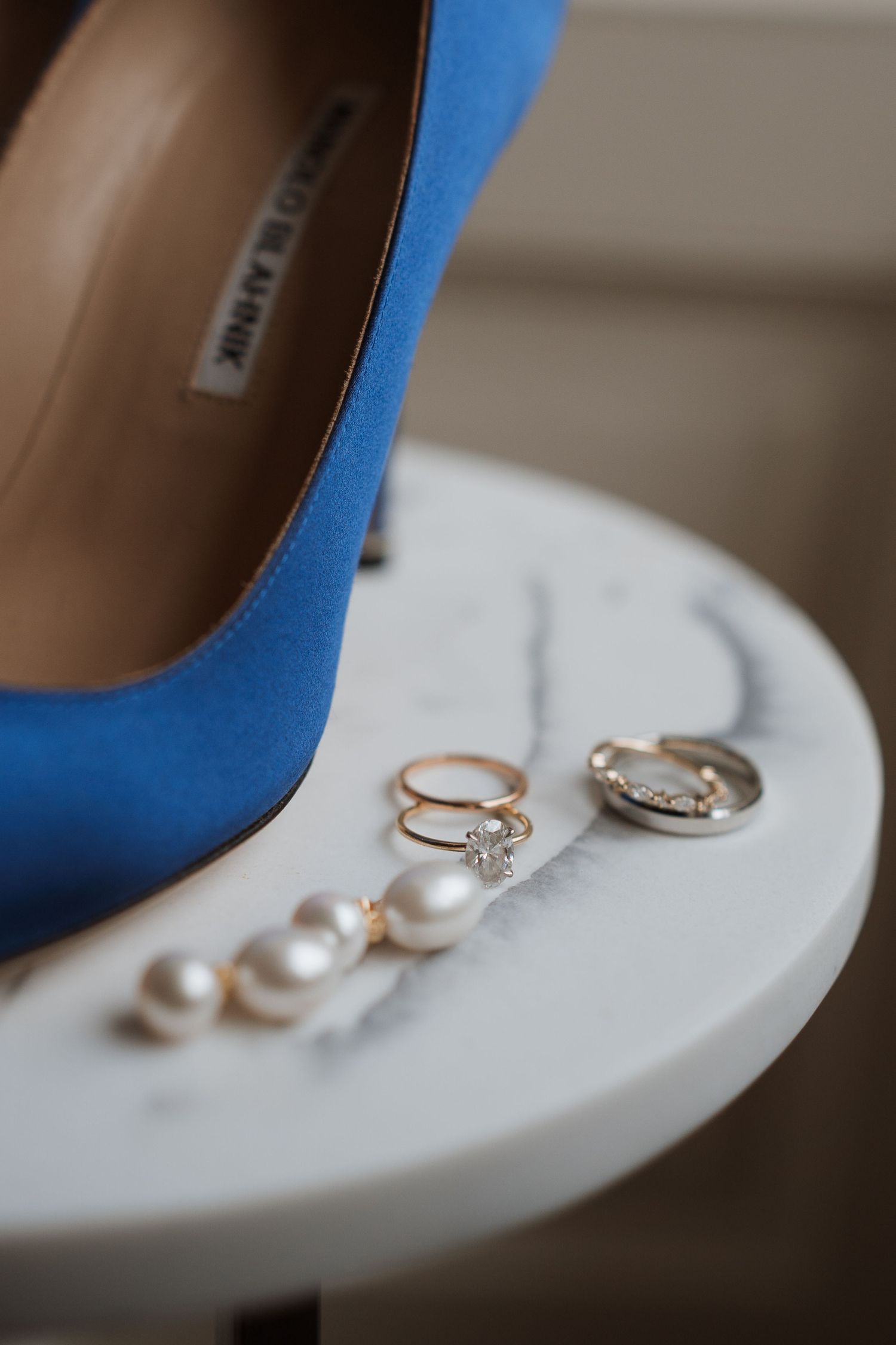 Blue wedding heel with engagement rings and pearl jewelry on white surface.