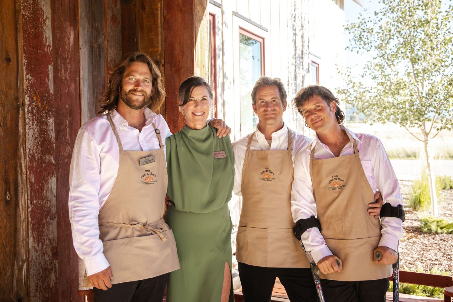 Group wearing matching khaki vests posing together in front of a rustic wooden structure.