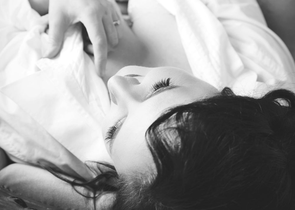 Black and white portrait of person lying on white bedding.